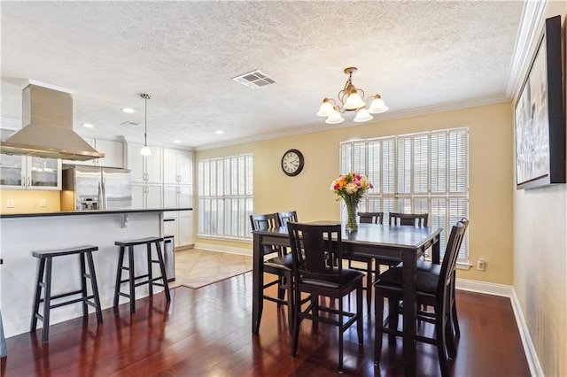 dining room with wood finished floors, baseboards, visible vents, a textured ceiling, and crown molding