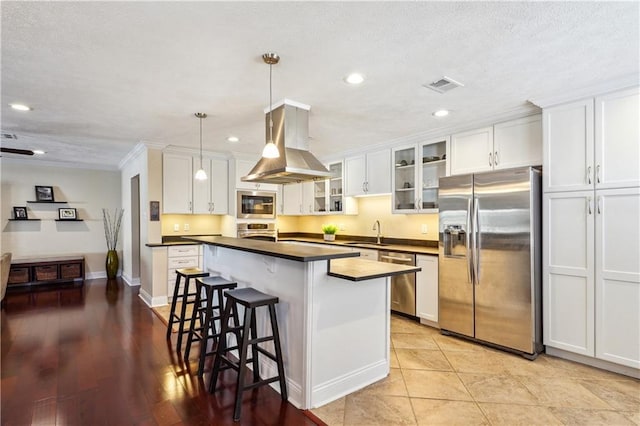 kitchen with visible vents, a kitchen bar, island exhaust hood, dark countertops, and appliances with stainless steel finishes