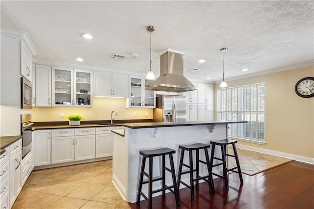 kitchen featuring visible vents, island exhaust hood, a sink, dark countertops, and stainless steel appliances