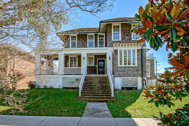 shingle-style home featuring covered porch, stairs, and a front yard