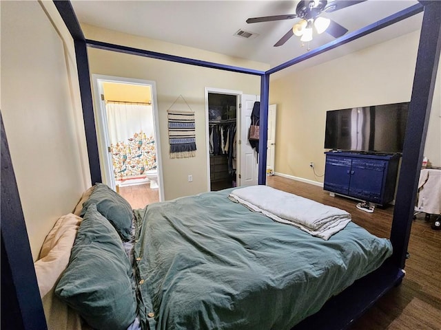 bedroom featuring visible vents, a walk in closet, baseboards, wood finished floors, and ensuite bath