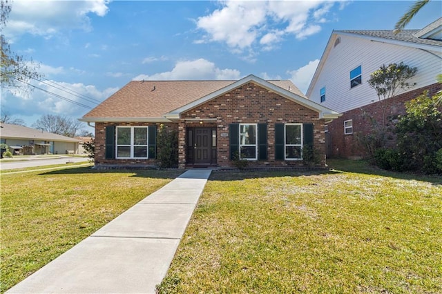 view of front of home featuring a front lawn, brick siding, and roof with shingles