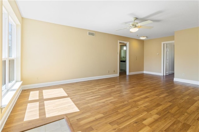 empty room featuring a ceiling fan, baseboards, visible vents, and light wood finished floors