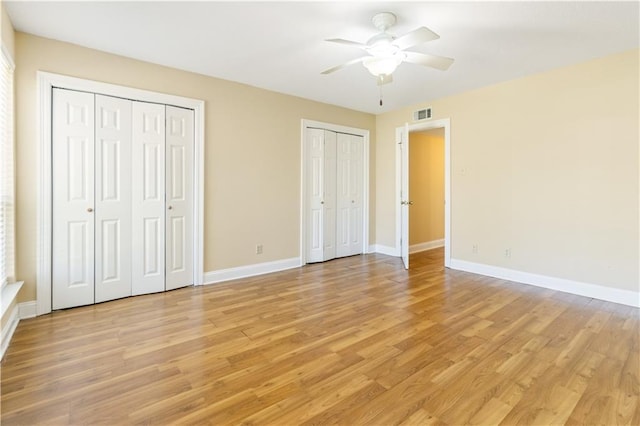 unfurnished bedroom with light wood-type flooring, visible vents, two closets, a ceiling fan, and baseboards