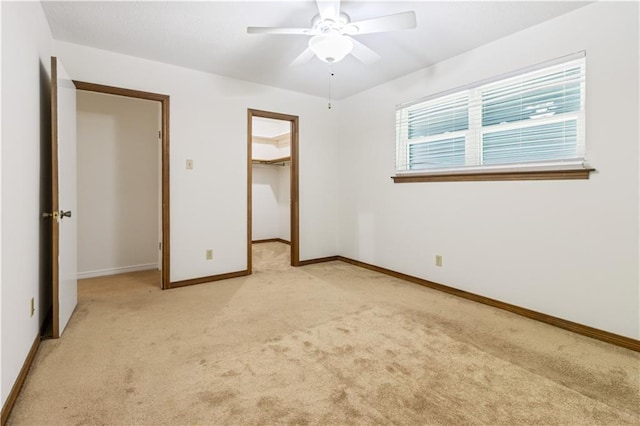 unfurnished bedroom with a walk in closet, baseboards, light carpet, a closet, and a ceiling fan