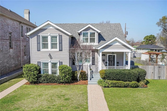 view of front of property featuring a porch, fence, a front lawn, and a shingled roof