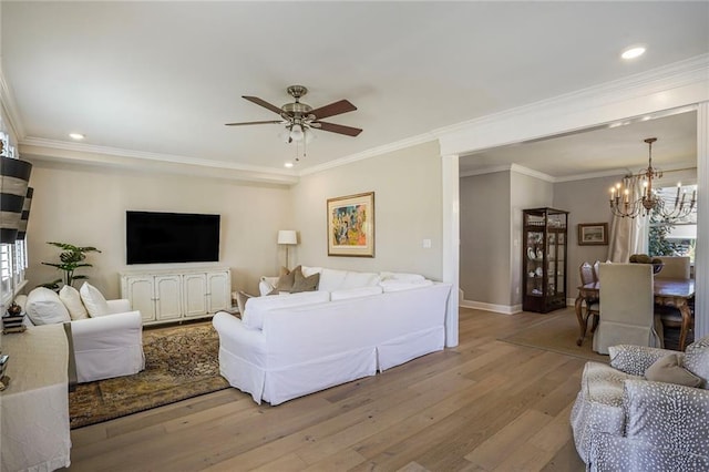 living area featuring crown molding, baseboards, ceiling fan with notable chandelier, wood finished floors, and plenty of natural light