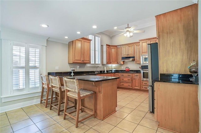 kitchen with a breakfast bar area, light tile patterned floors, a peninsula, appliances with stainless steel finishes, and under cabinet range hood