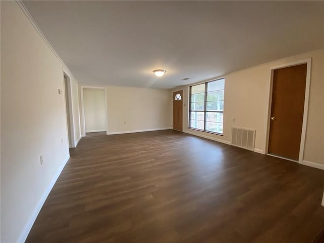 spare room with dark wood-style flooring, visible vents, and baseboards