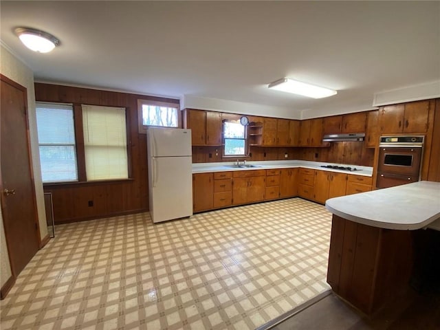 kitchen featuring under cabinet range hood, white appliances, wood walls, light countertops, and light floors