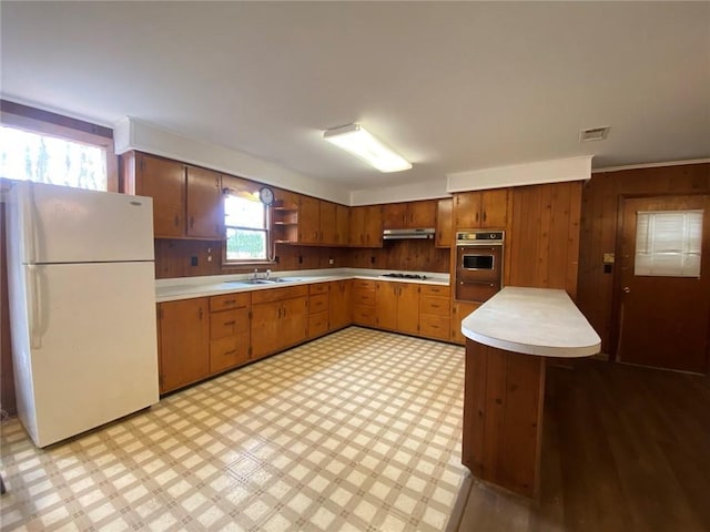 kitchen with oven, visible vents, under cabinet range hood, freestanding refrigerator, and light floors