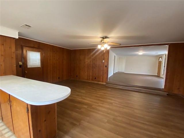 unfurnished living room with baseboards, wooden walls, a ceiling fan, visible vents, and wood finished floors