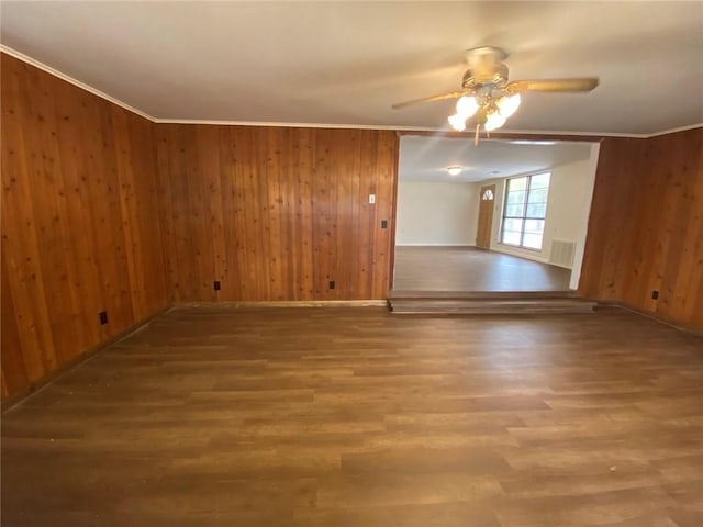 spare room featuring wooden walls, visible vents, a ceiling fan, and wood finished floors