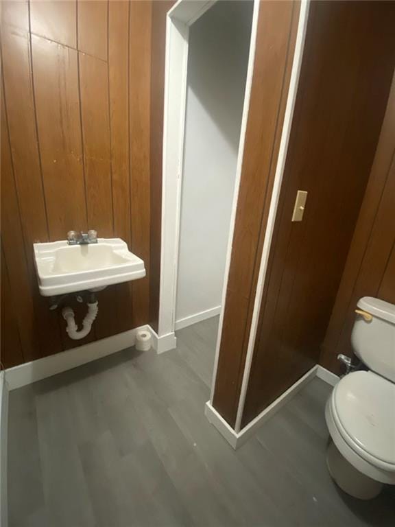 half bathroom featuring baseboards, wooden walls, toilet, a sink, and wood finished floors