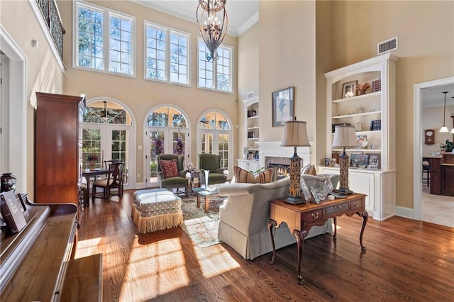 living room featuring visible vents, ornamental molding, a warm lit fireplace, wood finished floors, and an inviting chandelier