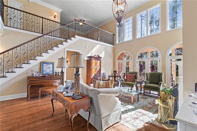 living area with baseboards, stairs, ornamental molding, an inviting chandelier, and wood finished floors