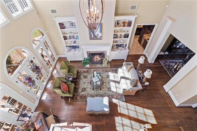 living room featuring wood finished floors, visible vents, a fireplace with flush hearth, and a towering ceiling