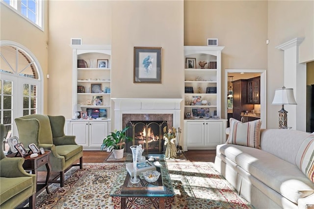 living room featuring a high end fireplace, visible vents, built in shelves, and a high ceiling