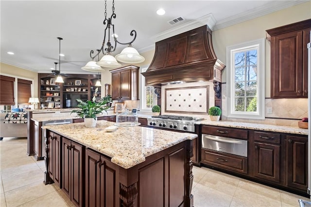 kitchen with a warming drawer, ornamental molding, custom range hood, a kitchen island, and stainless steel gas cooktop