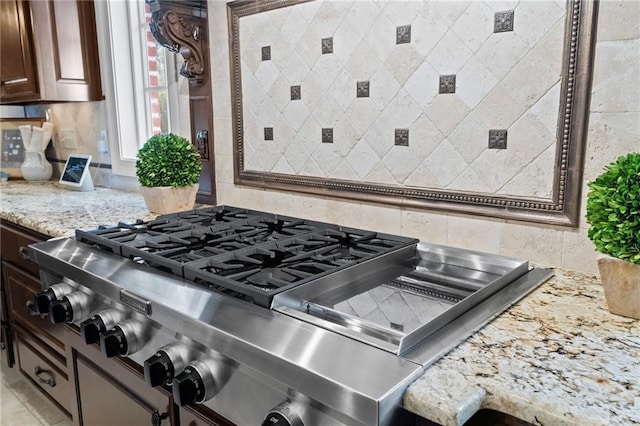 interior details with decorative backsplash, stainless steel gas stovetop, and light stone countertops