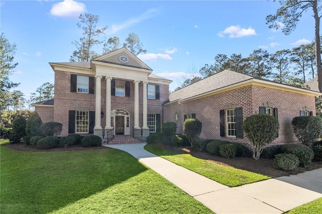 greek revival inspired property featuring brick siding and a front yard