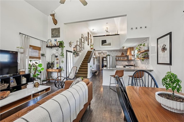 living area featuring stairway, dark wood-type flooring, a high ceiling, and a ceiling fan