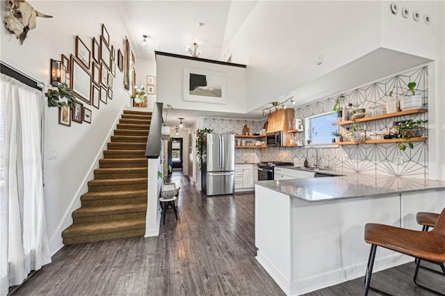 kitchen featuring open shelves, a peninsula, a sink, stainless steel appliances, and tasteful backsplash