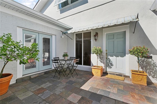 doorway to property with french doors, a patio, brick siding, and stucco siding