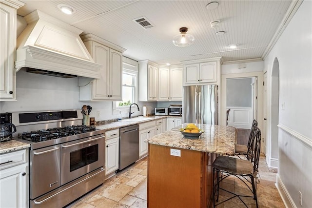 kitchen with visible vents, custom exhaust hood, a sink, stainless steel appliances, and a kitchen bar