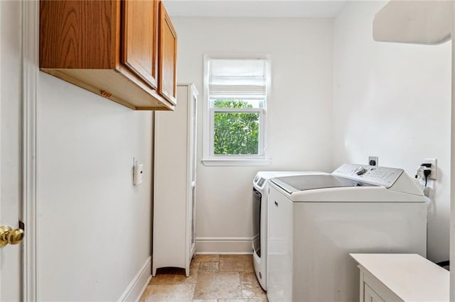 washroom with baseboards, cabinet space, stone tile floors, and washer and clothes dryer