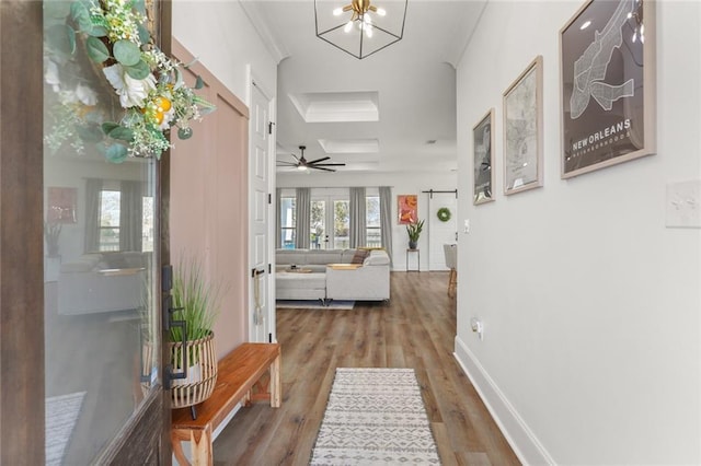 hallway featuring crown molding, baseboards, wood finished floors, a notable chandelier, and a raised ceiling