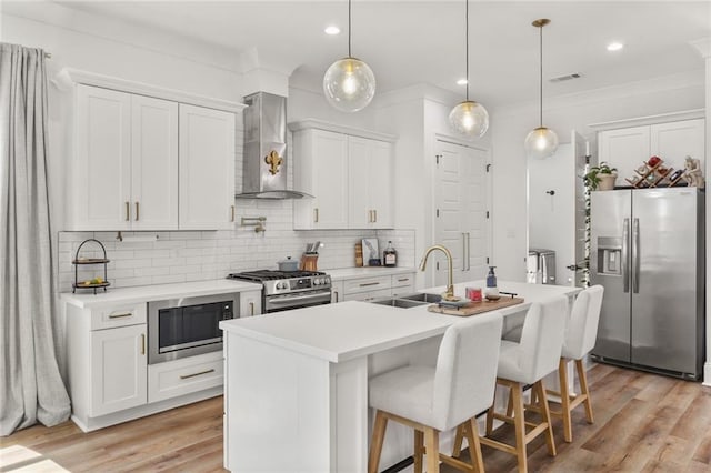 kitchen featuring visible vents, a sink, backsplash, appliances with stainless steel finishes, and wall chimney exhaust hood