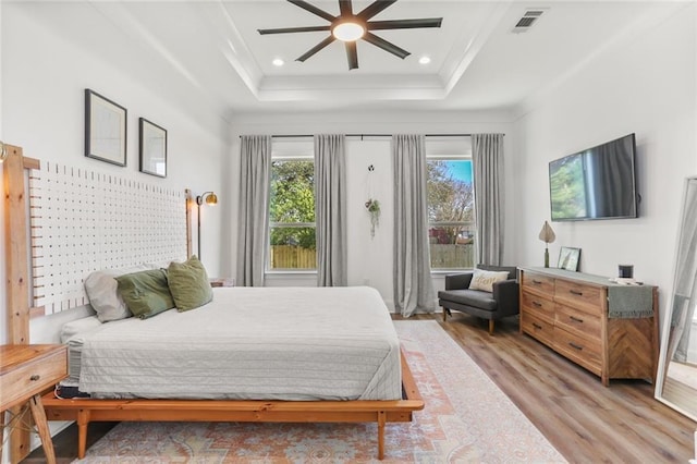 bedroom featuring wood finished floors, visible vents, a tray ceiling, recessed lighting, and ornamental molding