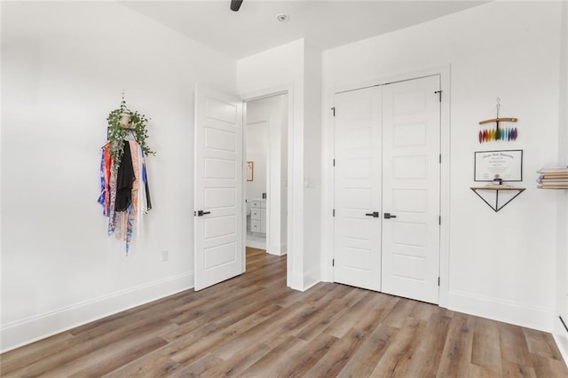 unfurnished bedroom with a ceiling fan, wood finished floors, baseboards, and a closet