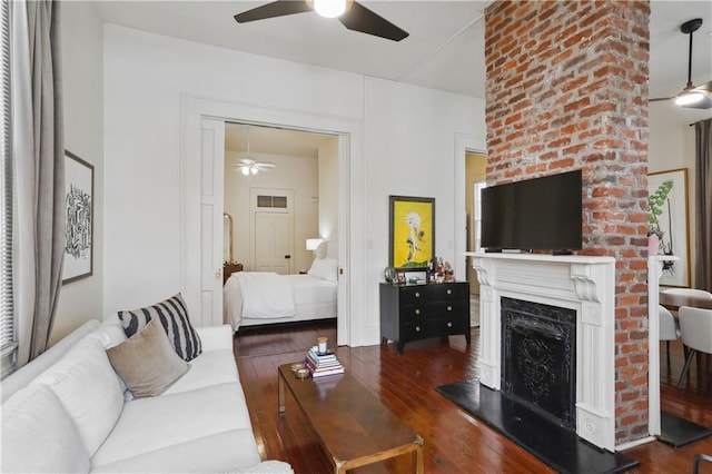 living area with a fireplace with raised hearth, ceiling fan, and wood-type flooring