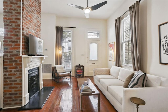 living area with visible vents, a brick fireplace, a ceiling fan, and dark wood-style flooring
