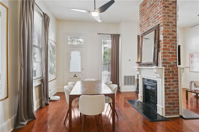 dining area with visible vents, a fireplace with raised hearth, baseboards, ceiling fan, and dark wood-style floors