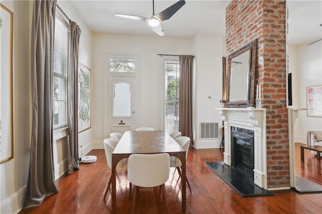 dining area with visible vents, a fireplace with raised hearth, baseboards, ceiling fan, and dark wood-style flooring