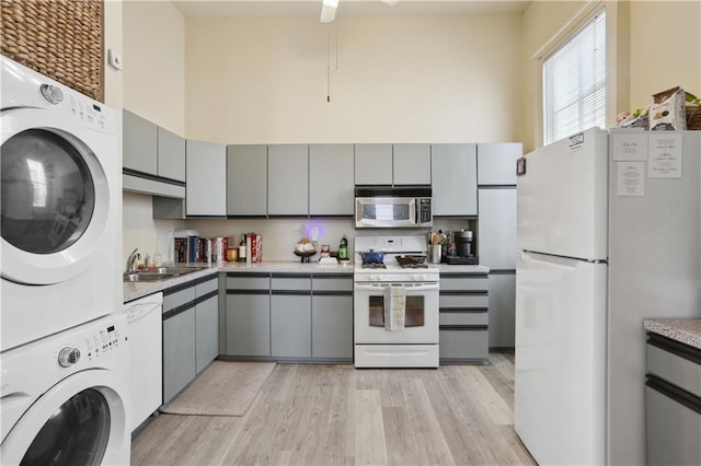 kitchen featuring white appliances, a sink, gray cabinetry, stacked washer and clothes dryer, and a towering ceiling