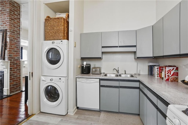 clothes washing area featuring laundry area, light wood-style flooring, a high ceiling, a sink, and stacked washer / dryer