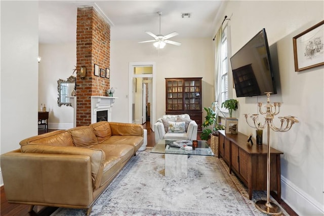 living room with visible vents, a brick fireplace, baseboards, ceiling fan, and wood finished floors