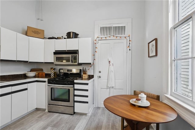kitchen featuring light wood-type flooring, stainless steel appliances, dark countertops, and white cabinetry