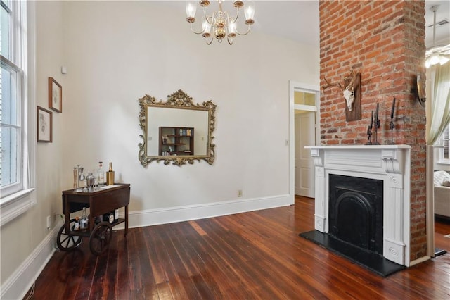 unfurnished living room with hardwood / wood-style flooring, a notable chandelier, a fireplace with raised hearth, and baseboards