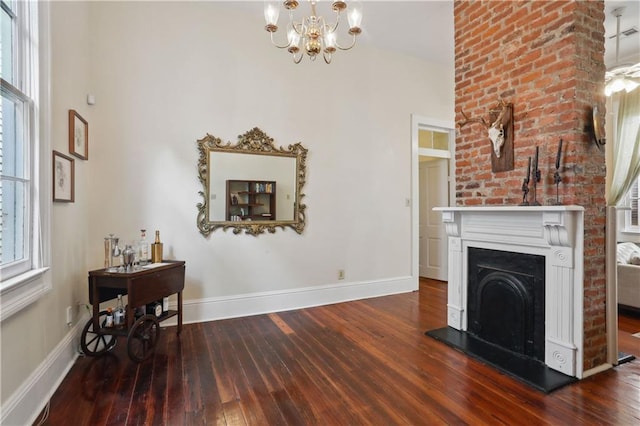 unfurnished living room featuring hardwood / wood-style floors, a notable chandelier, a fireplace with raised hearth, and baseboards