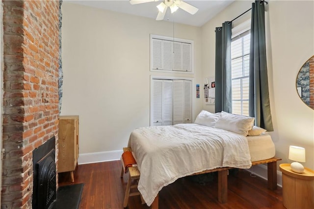 bedroom with hardwood / wood-style floors, a brick fireplace, a ceiling fan, and baseboards