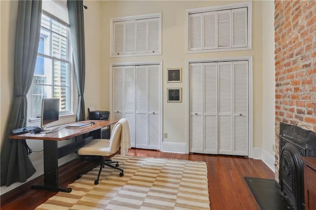 office space featuring hardwood / wood-style flooring, a fireplace, baseboards, and a towering ceiling