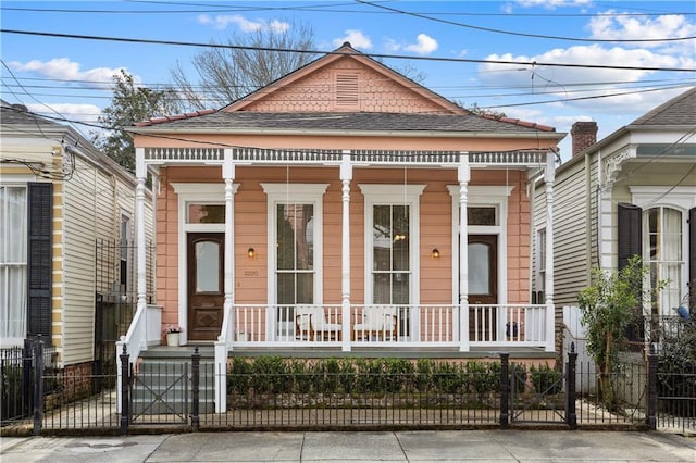 shotgun-style home featuring a fenced front yard, covered porch, roof with shingles, and a gate