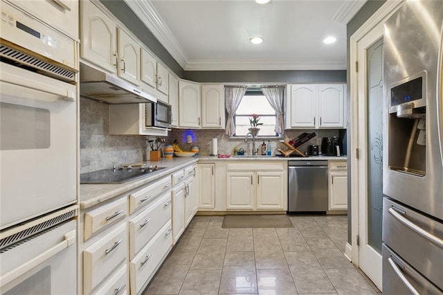 kitchen with a sink, under cabinet range hood, appliances with stainless steel finishes, crown molding, and light countertops