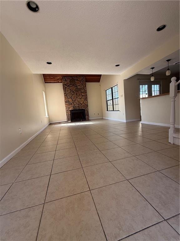 unfurnished living room featuring a stone fireplace, light tile patterned floors, baseboards, and a textured ceiling