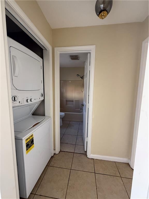 laundry area with light tile patterned flooring, laundry area, stacked washing maching and dryer, and baseboards